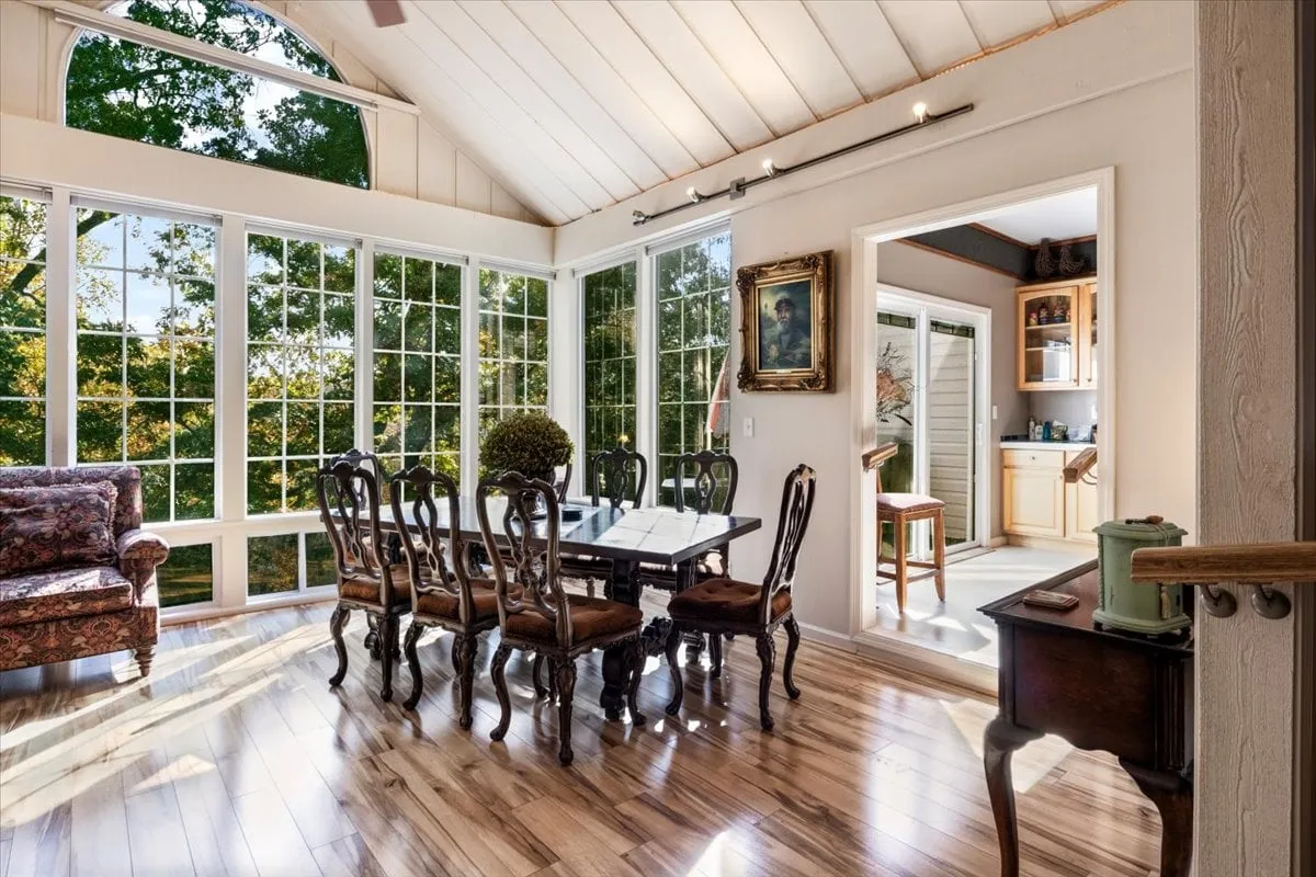 A warmly decorated dining room highlighted by a large window flooding the space with natural light, an inviting dining table set for family or group meals, a floral-patterned sofa adding charm, and curated wall artwork. The overall mood is festive yet intimate, ideal for memorable dinners.