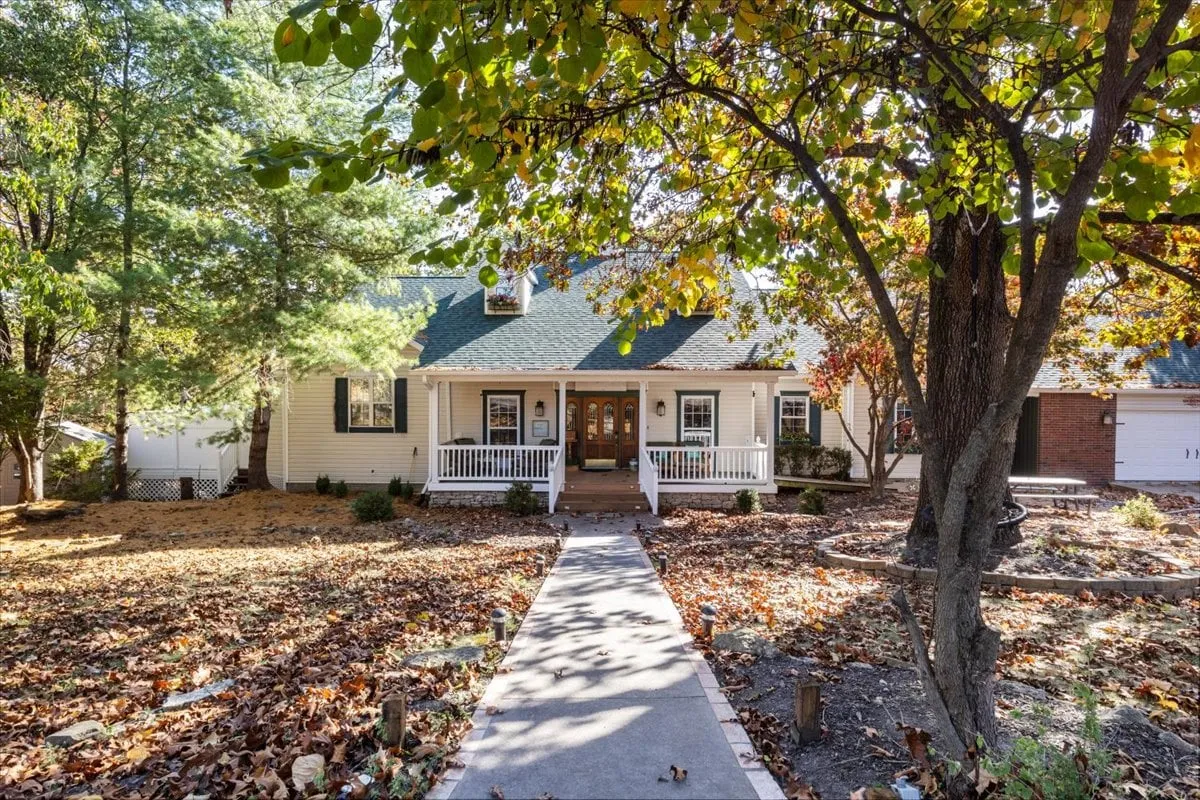 A welcoming front porch surrounded by lush greenery, with inviting seating and a charming pathway leading up to the house. The scene is bathed in natural light, highlighting the porch as an ideal spot for relaxing or gathering with friends and family.