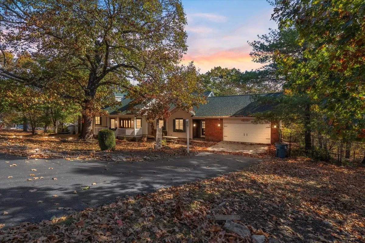 A tranquil exterior image showcasing the house, a large tree, and a driveway blanketed in autumn leaves. The cozy atmosphere is perfect for outdoor relaxation, family gatherings, and barbecues, with the porch and surrounding yard visible.