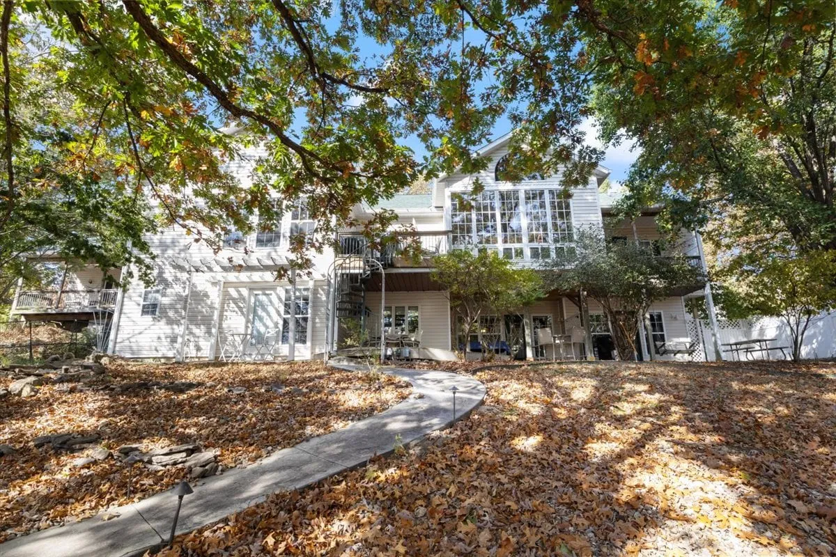 An exterior view showcasing large windows, a graceful spiral staircase, and lush surrounding trees with a welcoming pathway. The home blends seamlessly into its natural setting, inviting guests to explore the grounds and enjoy the changing seasons.
