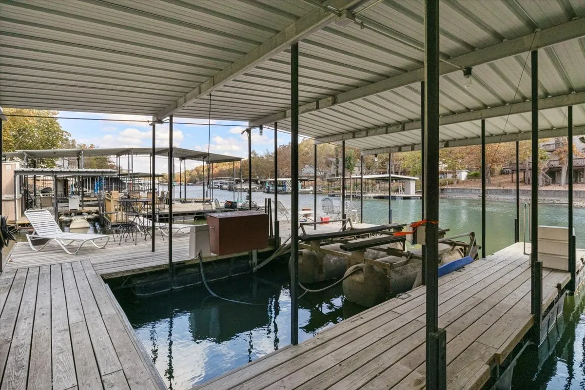 Wooden docks lined with moored boats stretch out over the calm water. The scene captures the leisurely pace of lakeside life, with reflections shimmering on the surface and canopy structures offering shade. The atmosphere is serene and inviting, ideal for fishing or unwinding by the water.