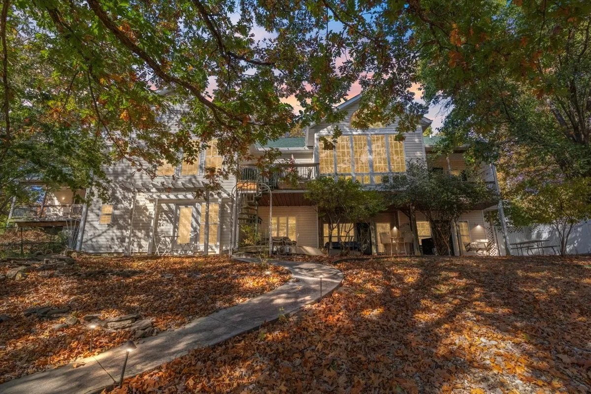 A broad view of the house with a spiral staircase, colorful autumn trees, and a winding pathway. The patio and yard invite exploration, family gatherings, and casual outdoor conversations, especially as the sun sets.